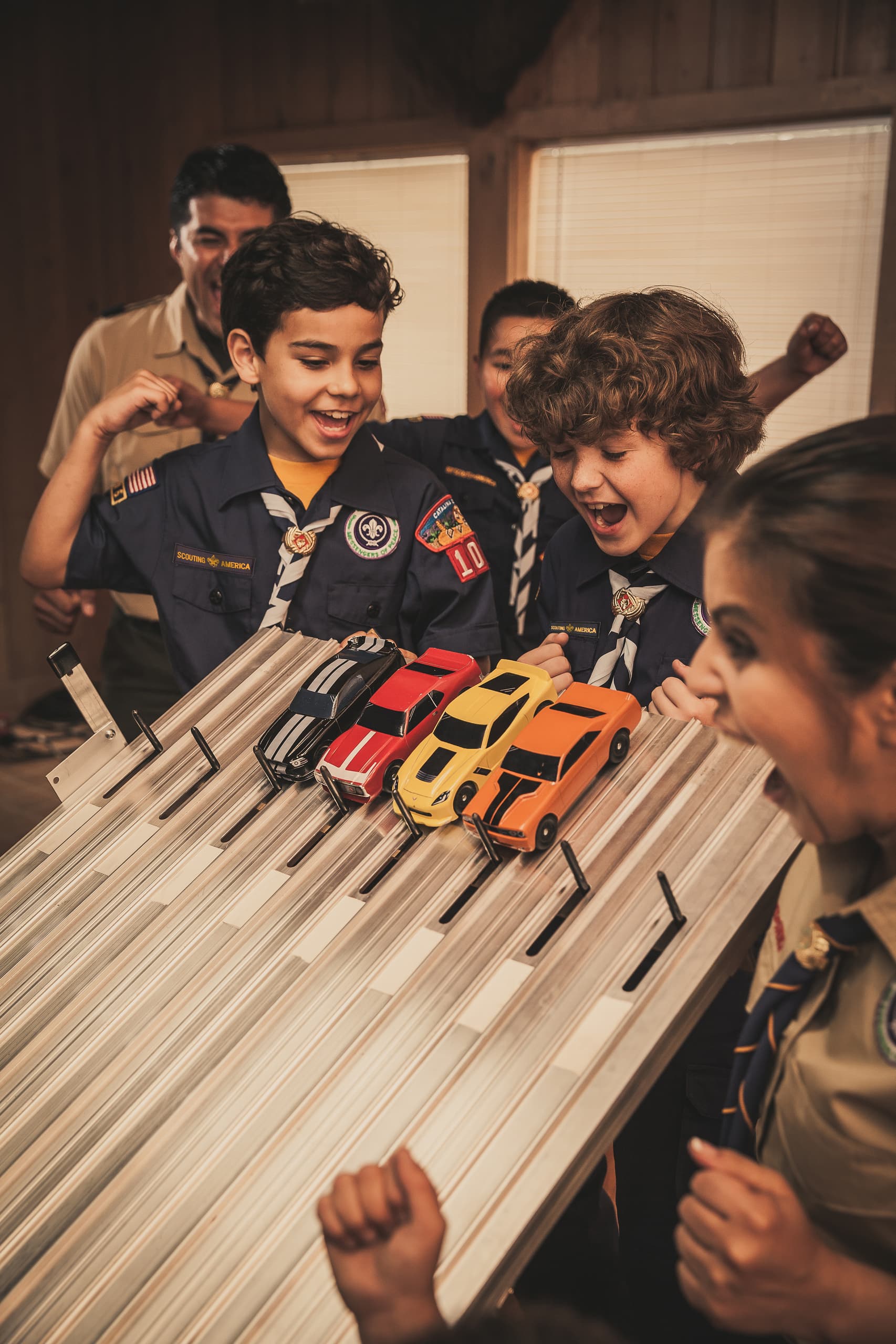 Scouts gathered around Pinewood Derby cars and a race track.
